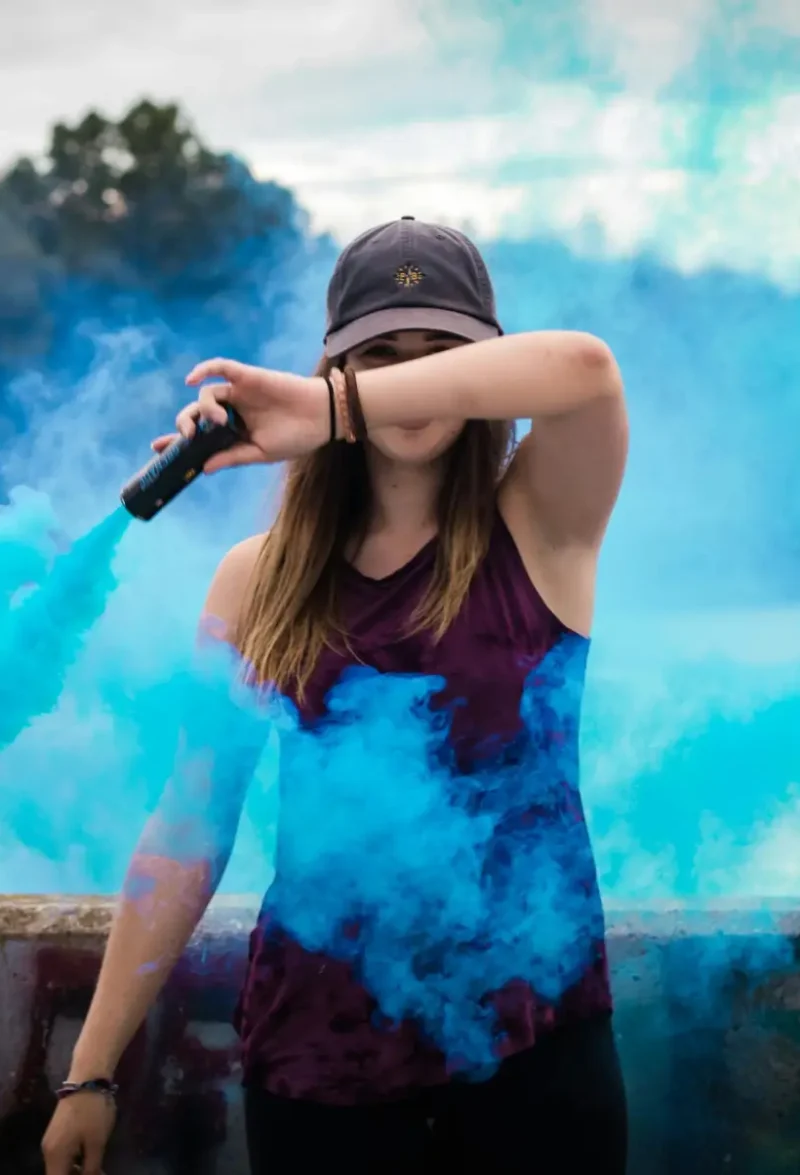 A stylish woman surrounded by bright blue smoke outdoors, creating a dynamic fashion statement.